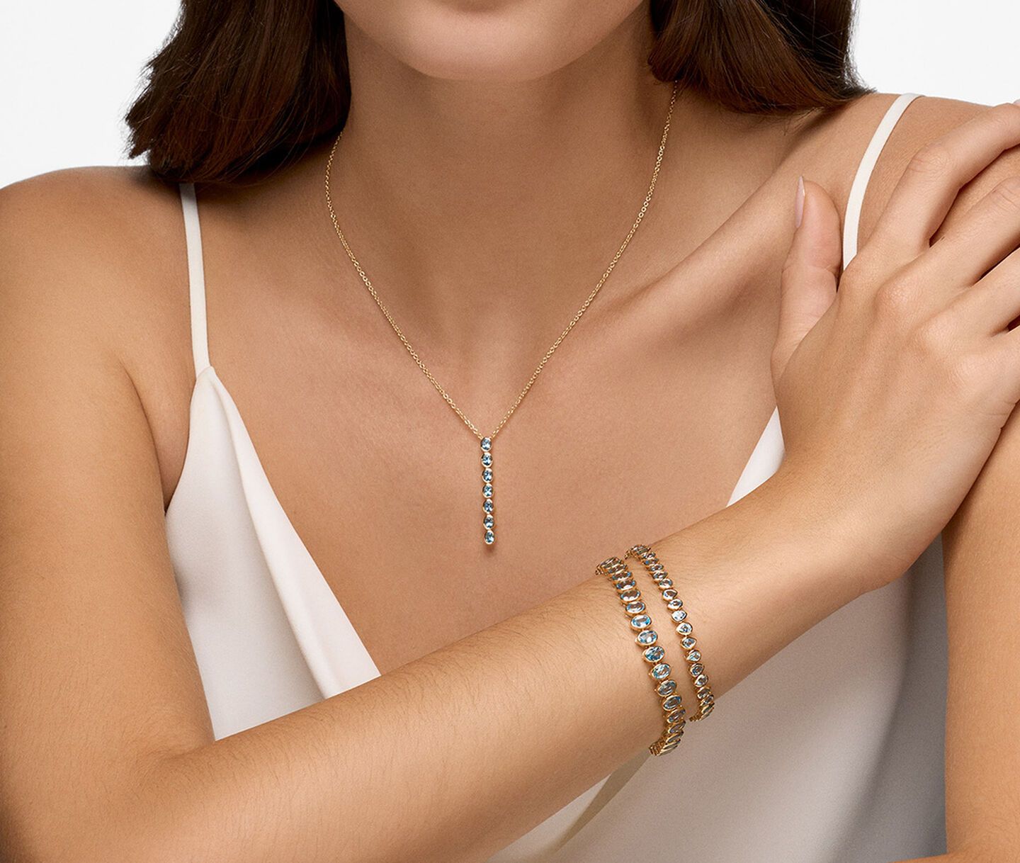 A woman wearing topaz and gold bracelets and necklace.